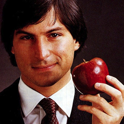 Steve Jobs dressed in suit holding a red apple.